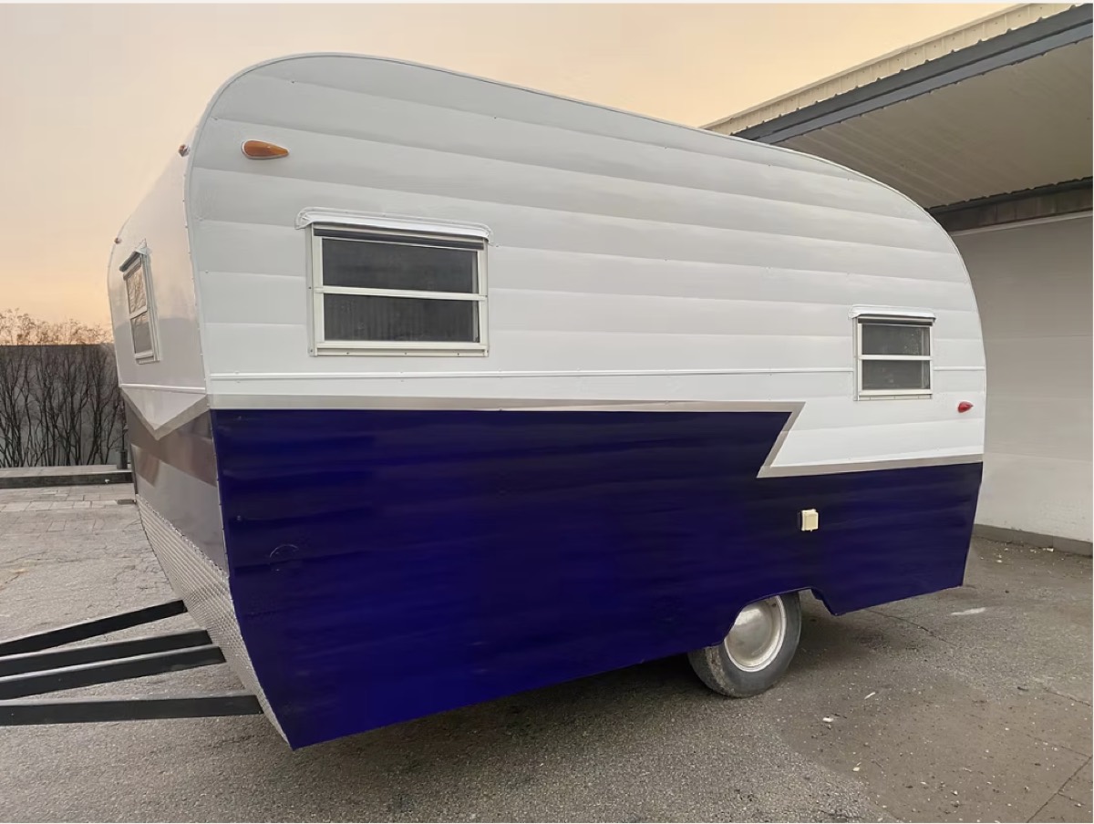 A vintage canned ham trailer finished in white and deep blue ribbed aluminum siding