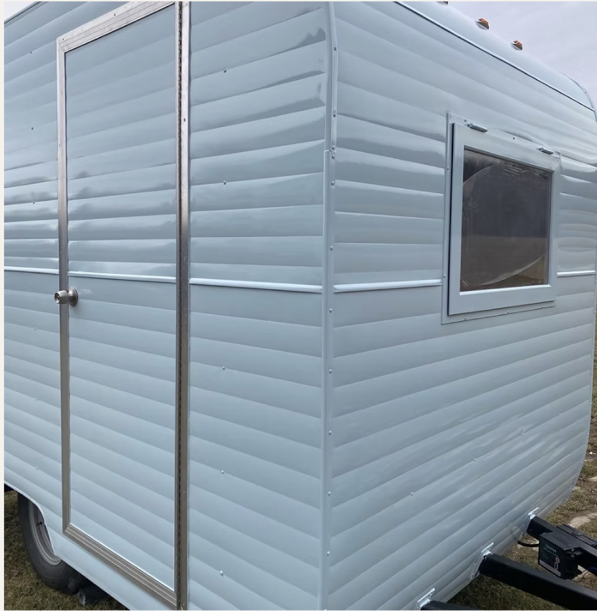Close-up of pale blue ribbed aluminum siding on a restored trailer, with polished trim