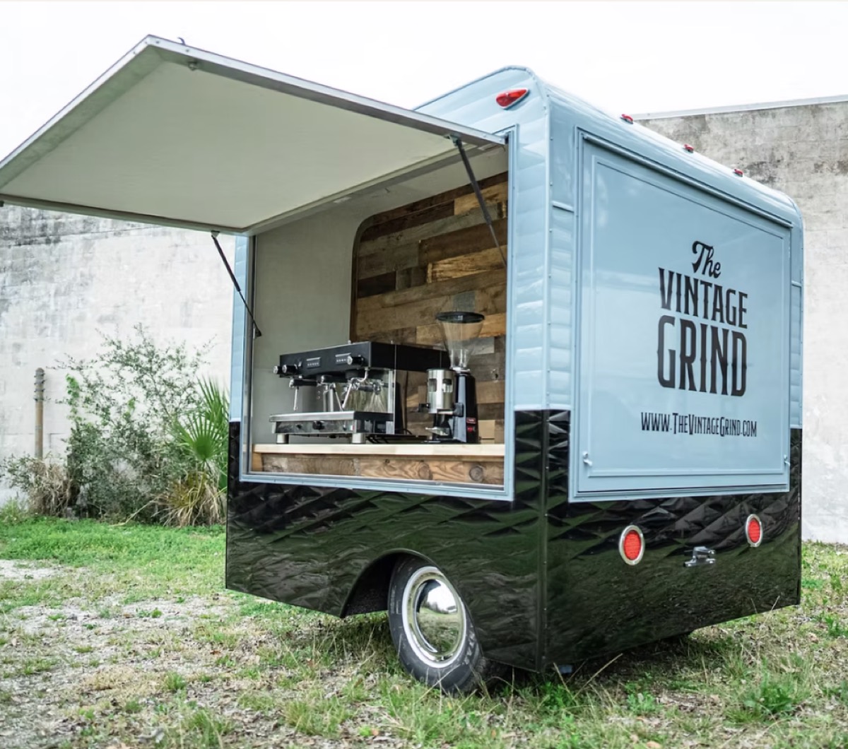 A coffee trailer clad in black diamond-pattern aluminum with a seafoam upper body